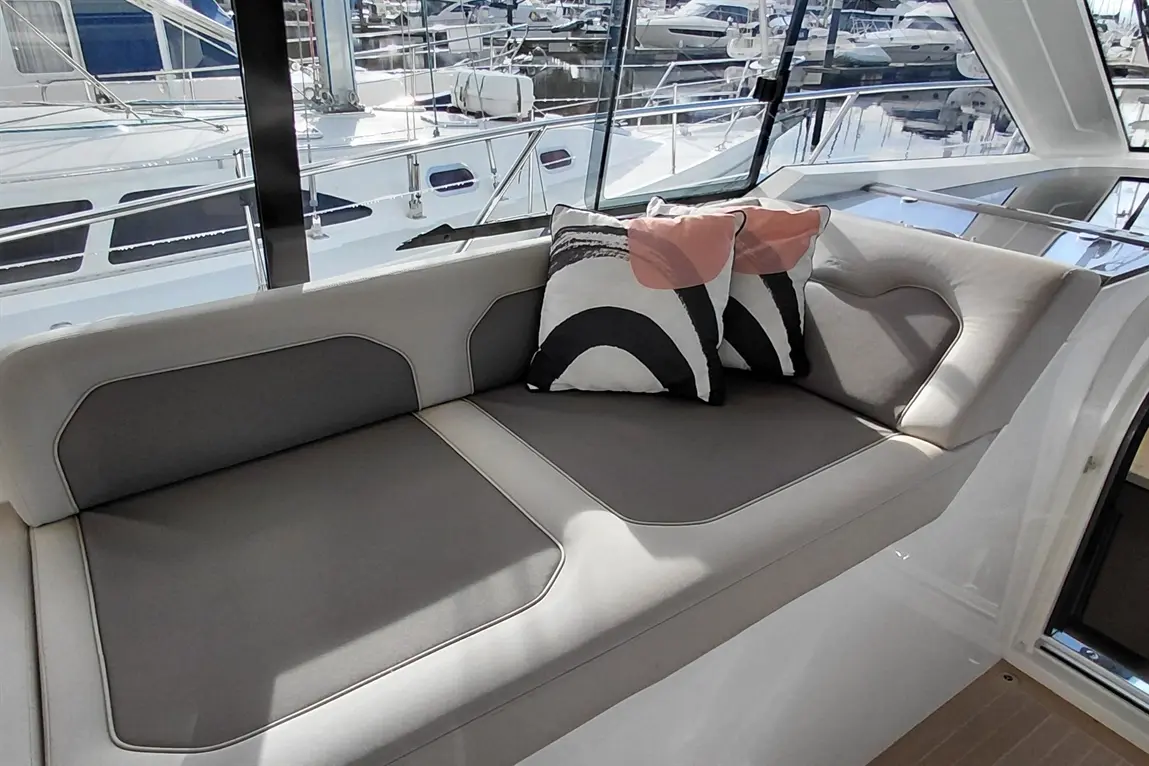 Stylish grey and cream boat seating adorned with black and pink geometric cushions, overlooking a marina filled with yachts.